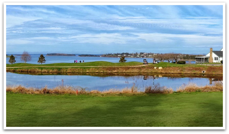 View of golf course surrounded by ocean with a white building and golf carts in view