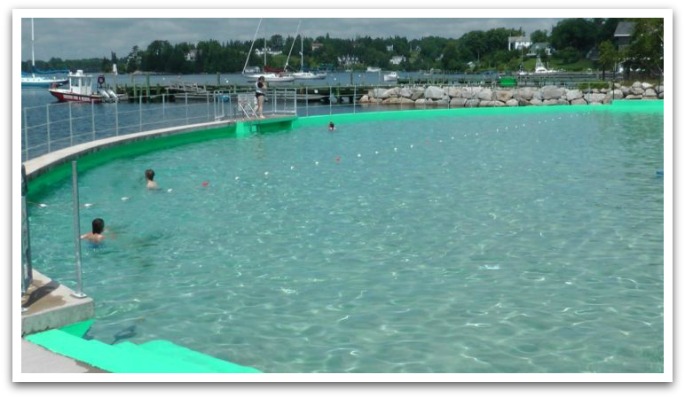 Lido pool with a wharf, ocean, and boats in the background