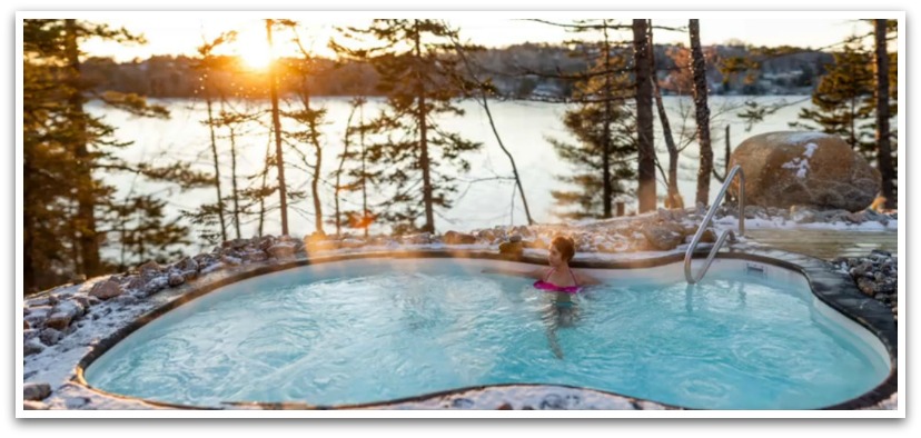 Woman relaxing in a small pool. Snow dusted ground with trees and ocean in the background at sunset.