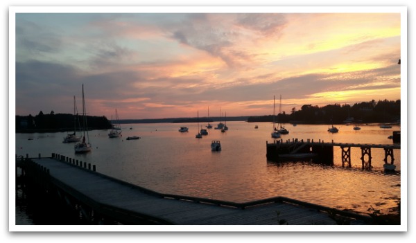 Sunset through clouds on Chester's back harbour which has silhouettes of boats and a wharf in the ocean.