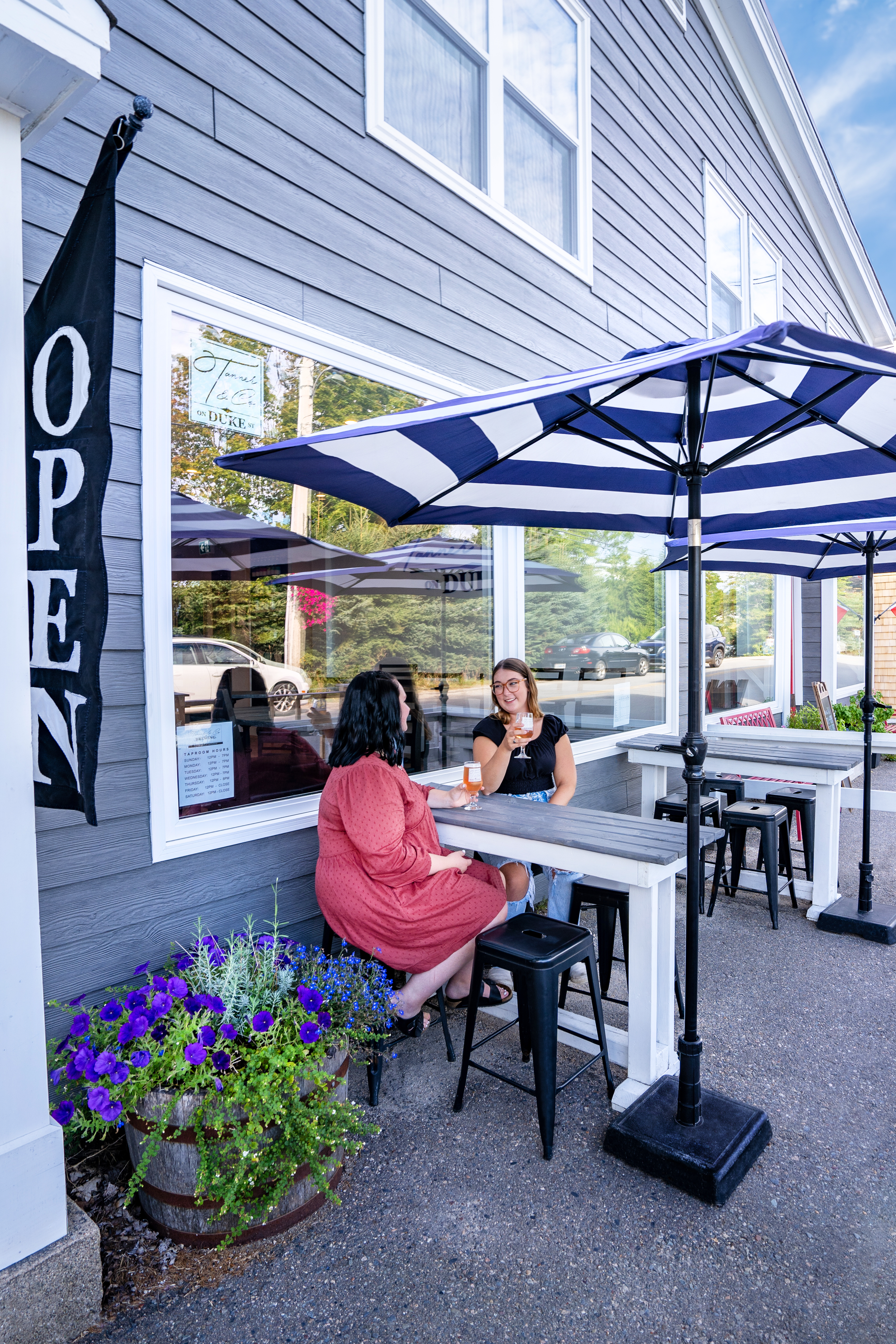 Two women sitting at a high table under a blue striped umbrella outside Tanner Brewery on Duke Street.