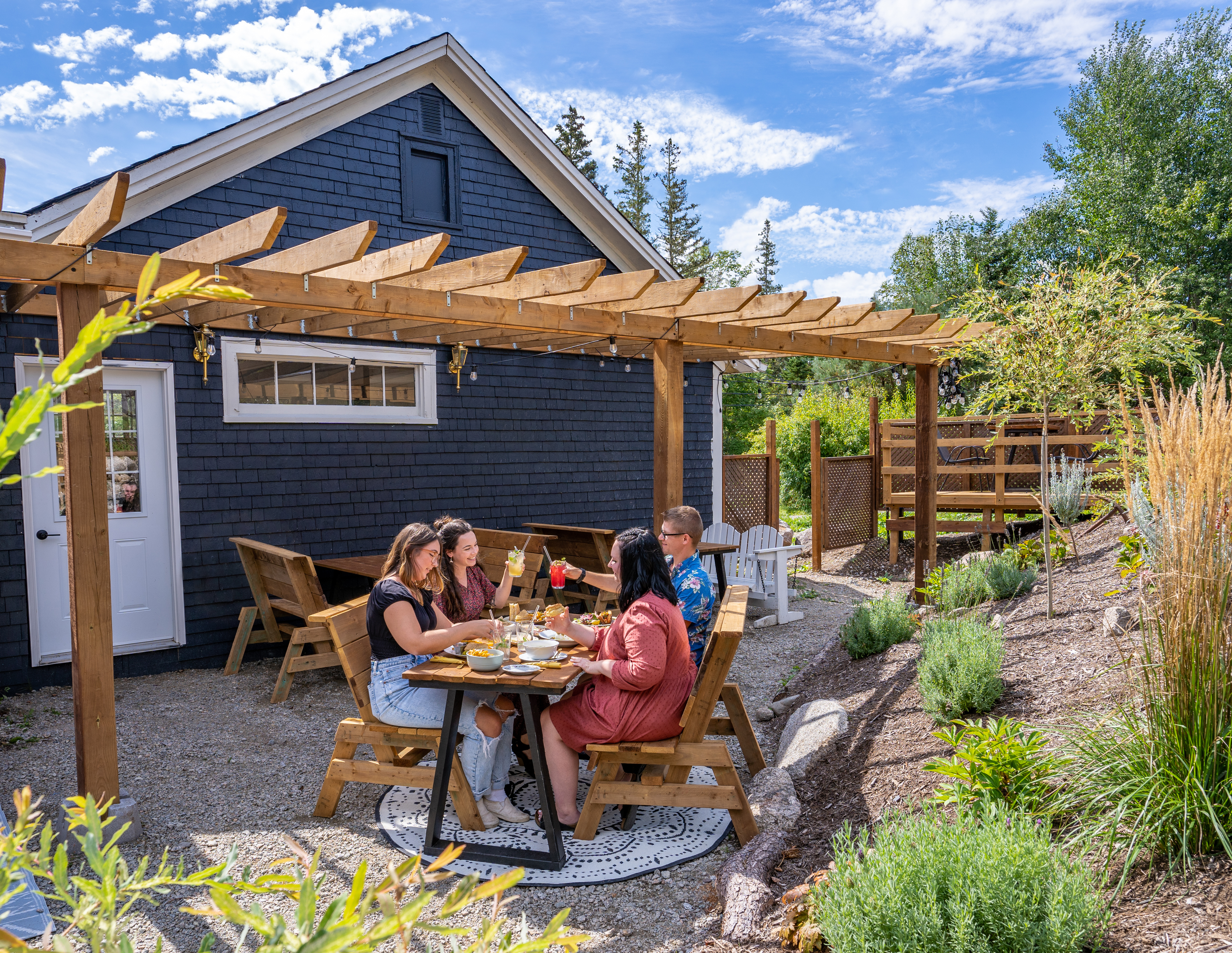 A group sitting outside Rosa Rugosa under stringed fairy lights with food and cocktails.