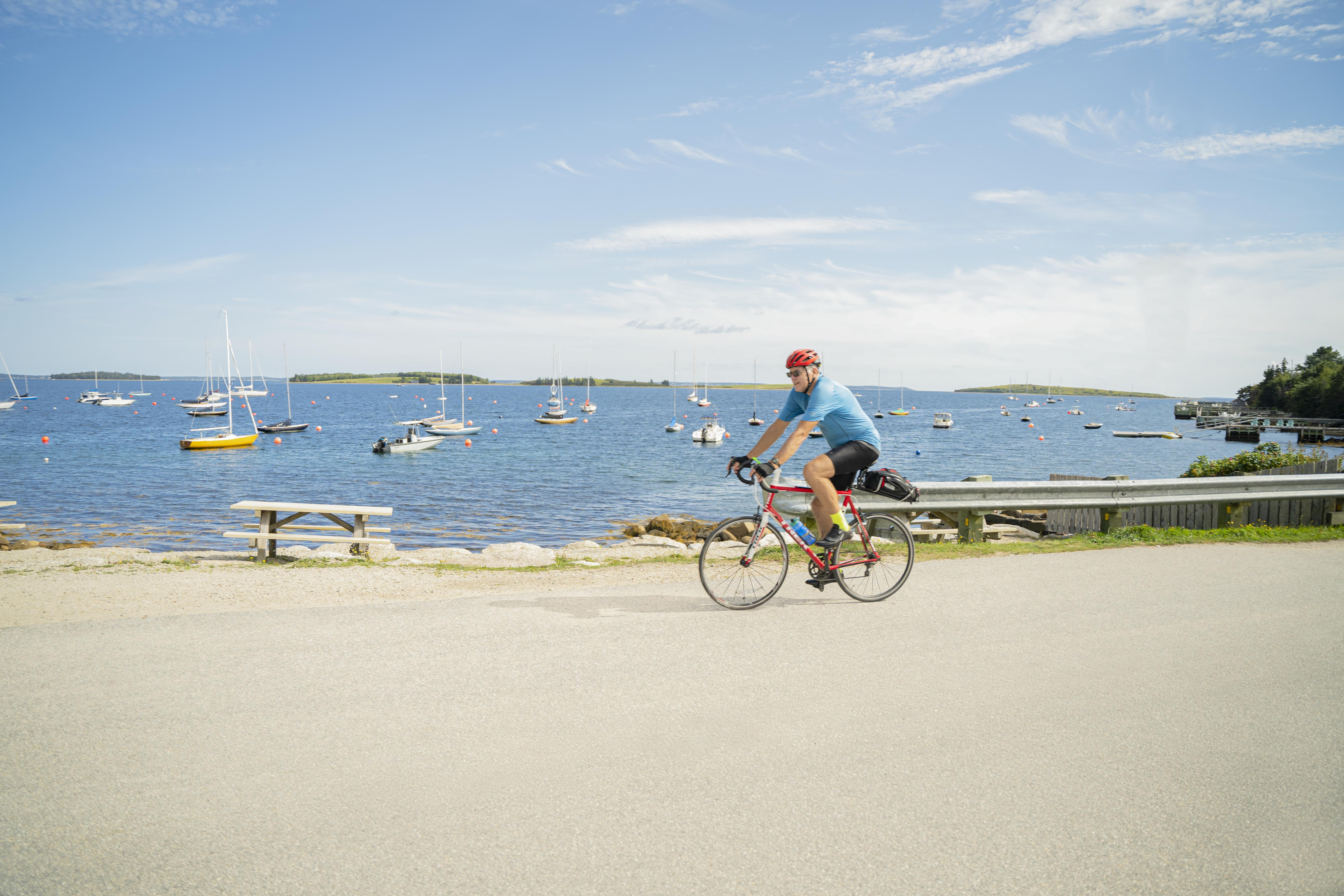 Person cycling along the coast with sail boats in the background