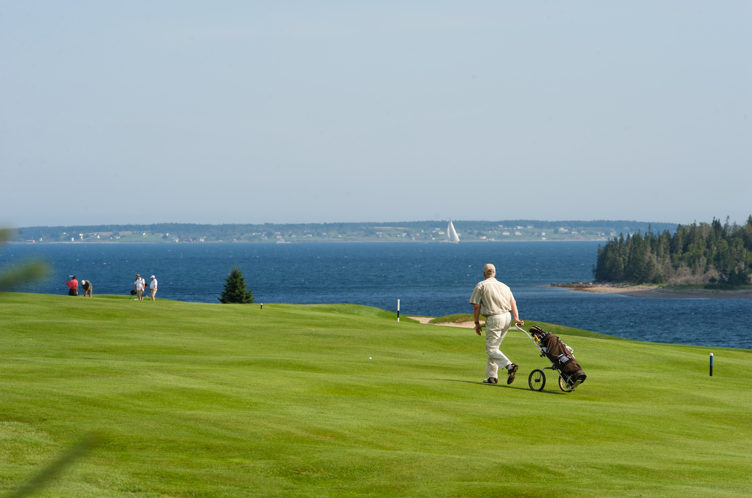 Photo of a person walking with a golf bag at Chester Golf Club, ocean in the background