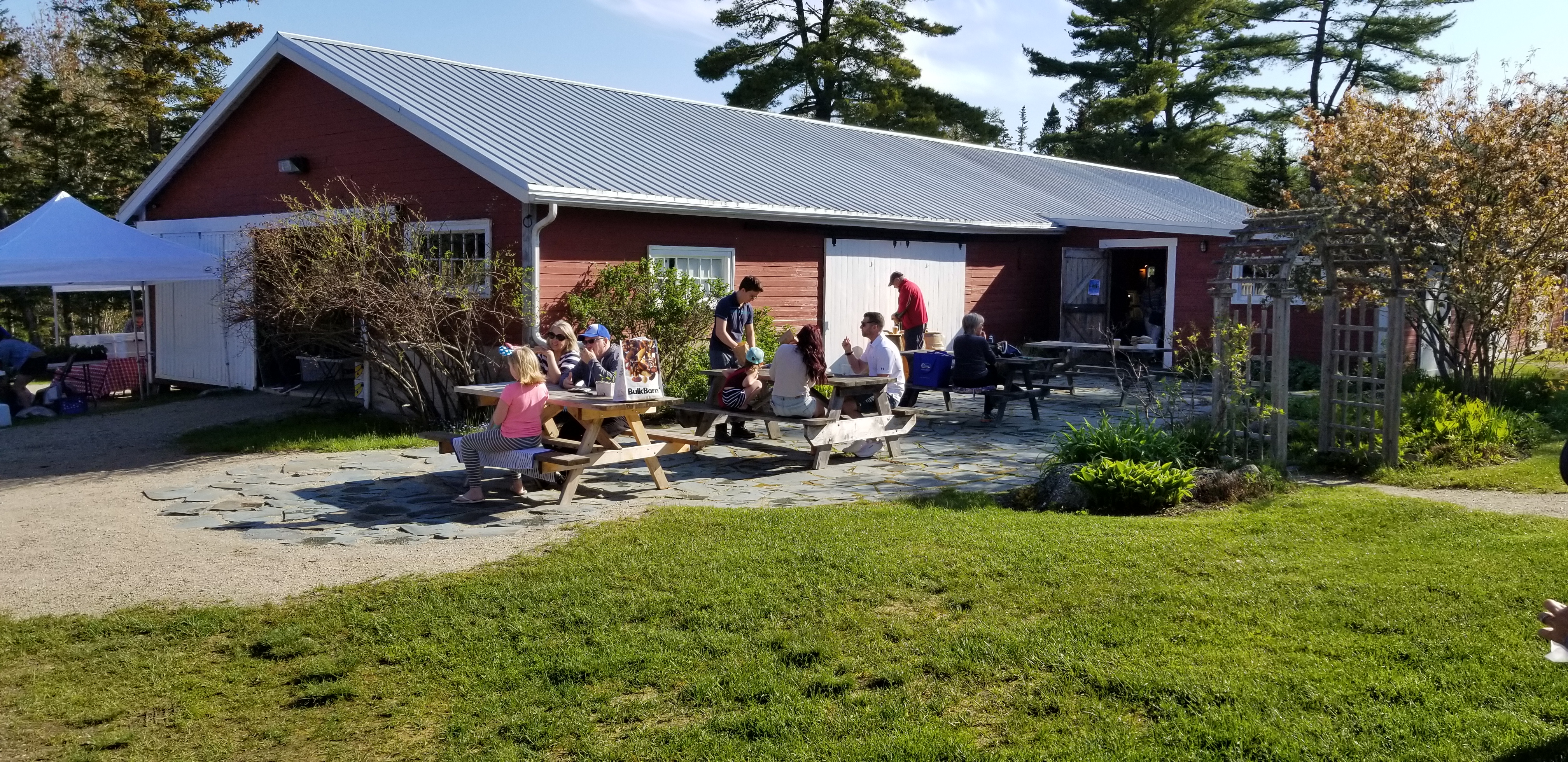 Photo of the back of the Hubbards Barn Farmers' Market with picnic tables, green grass, tents and the Hubbards Barn