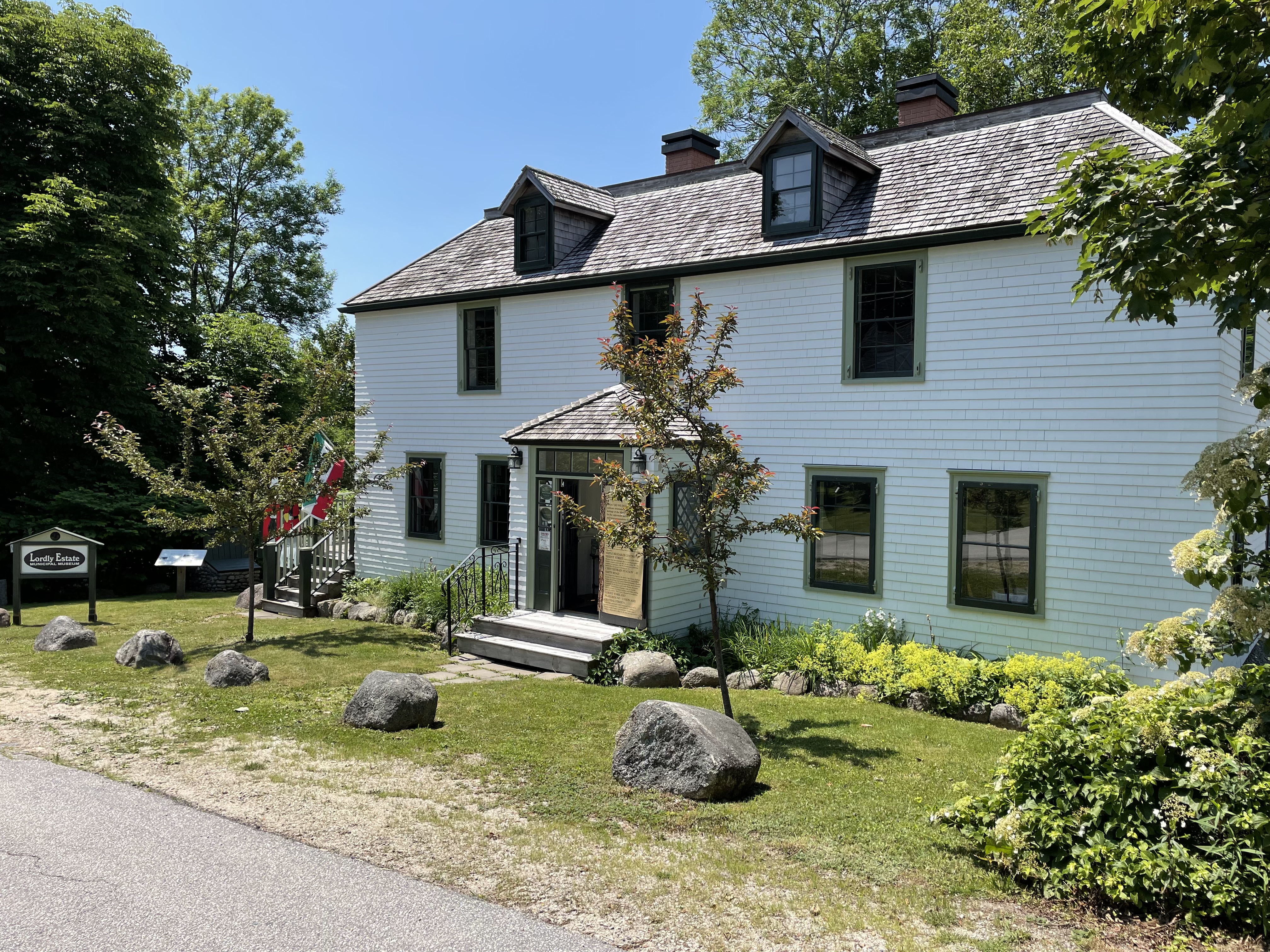 Picture of Lordly House, two stories, white with green trim, trees and garden out front