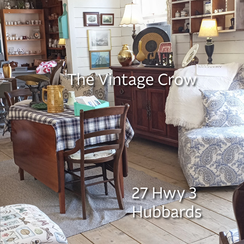 Photo showing a small dining table with chairs, a plush chair, and various antiques in the background