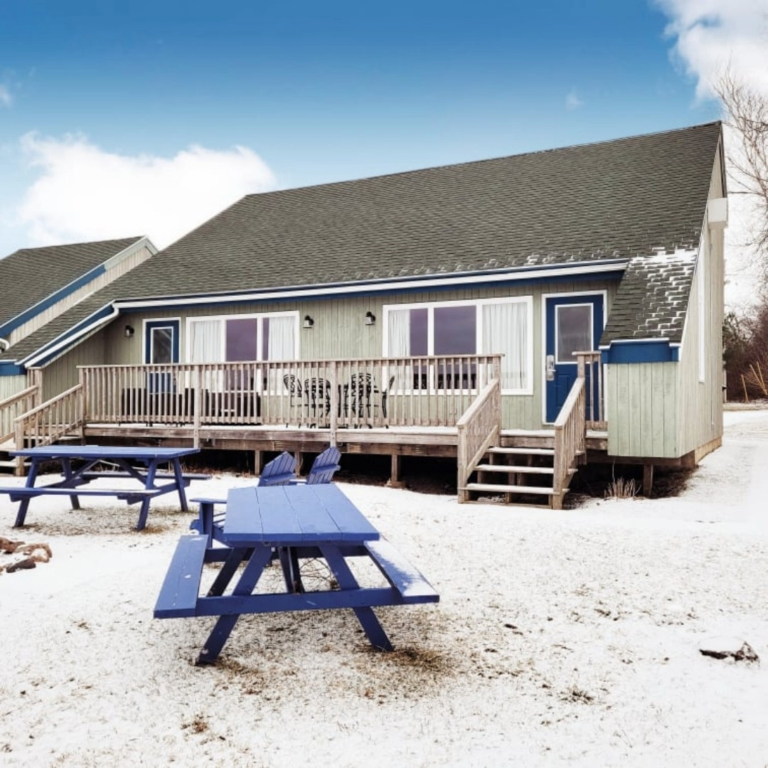 Photo of a cabin with a deck lightly covered in snow with a picnic table in front.