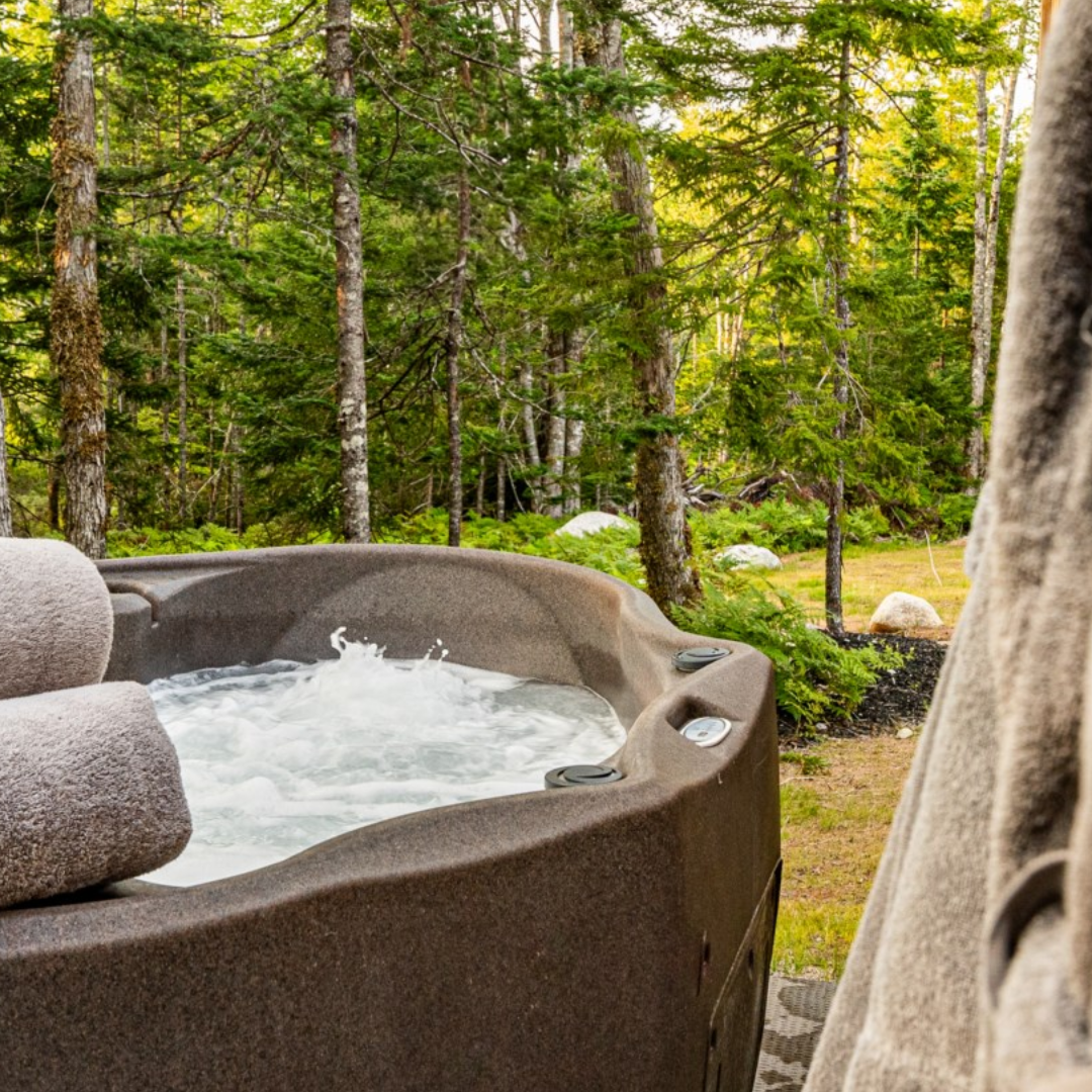 Photo shows a hot tub with towels and a robe on the side with trees in the background.