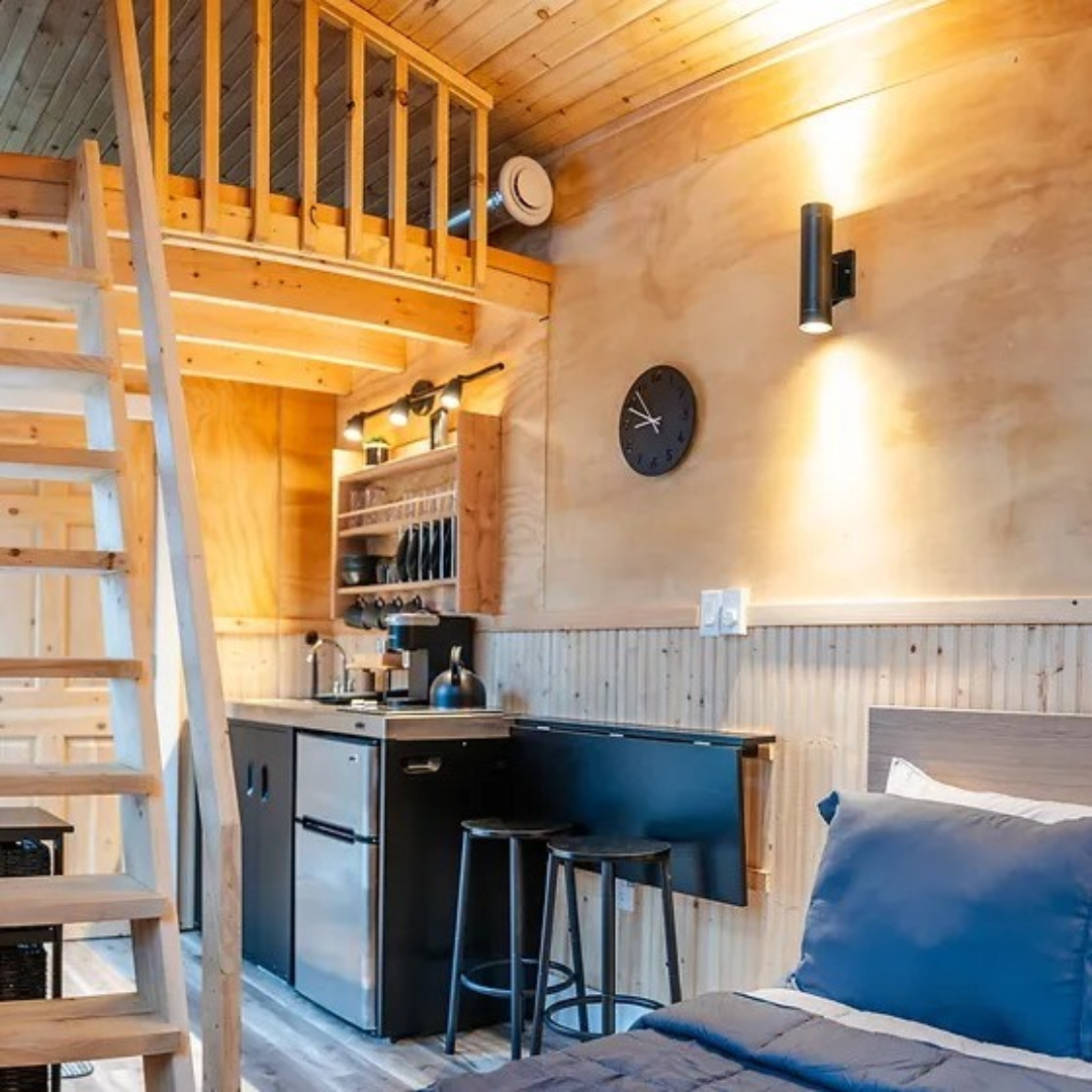 Photo shows the inside of one of the units with golden wood walls, bed, small kitchen, and loft space., 