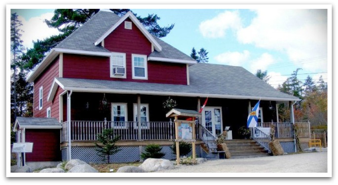 Exterior of the red Aspotogan heritage trust building with Nova Scotian and Canadian flags flying.