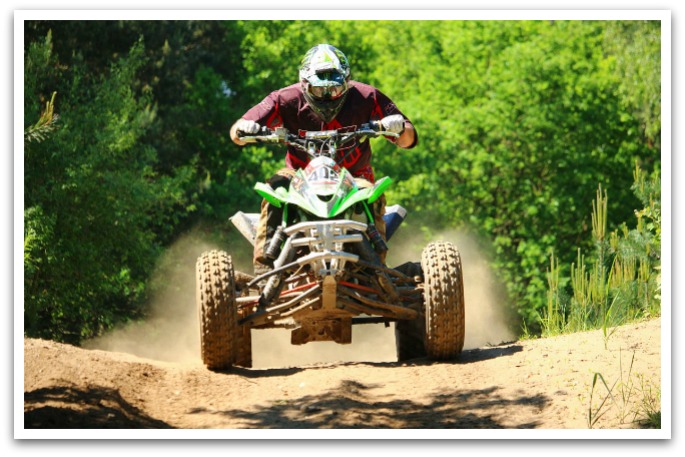Man wearing helmet on a green ATV on a dirt trail.