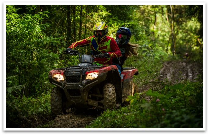 Man and woman on an ATV off-roading wearing bright coloured protective gear and helmets.