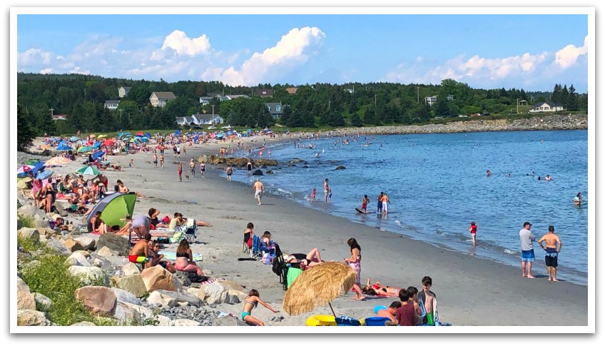 Many people sat on a beach with umbrellas