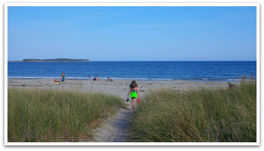 Girl in green walking down sand path with tall grass either side to Bayswater beach.