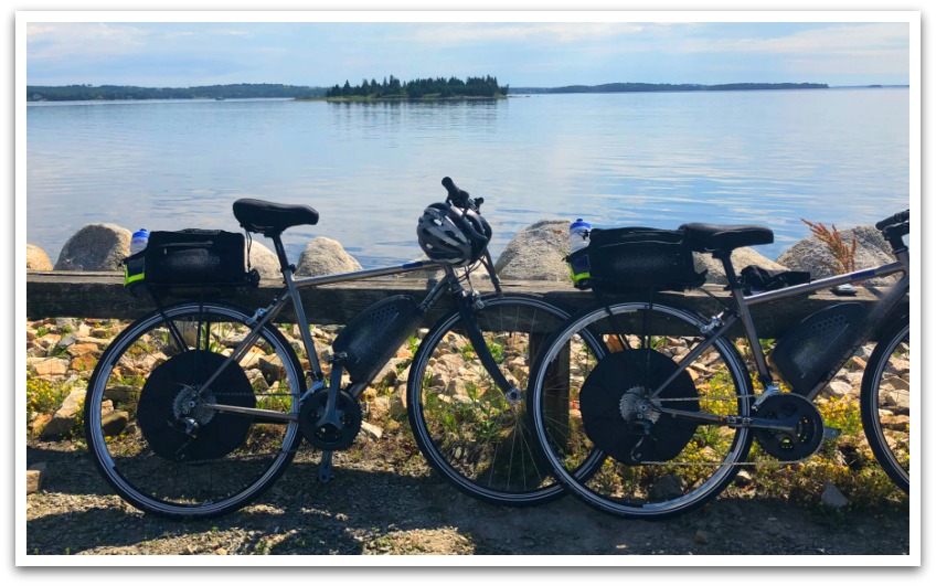 Two bicycles leaning against a rail facing vast waters with a forested island