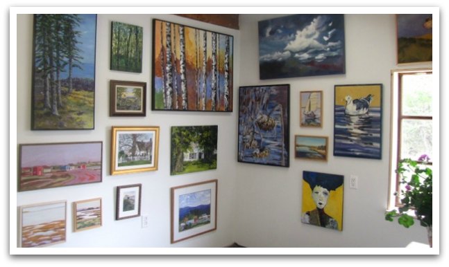 Collection of landscape and home paintings on white walls.