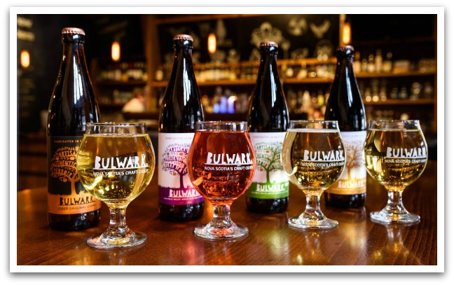 Four bottles of different flavours of Bulwark ciders with a glass of cider in front of each.