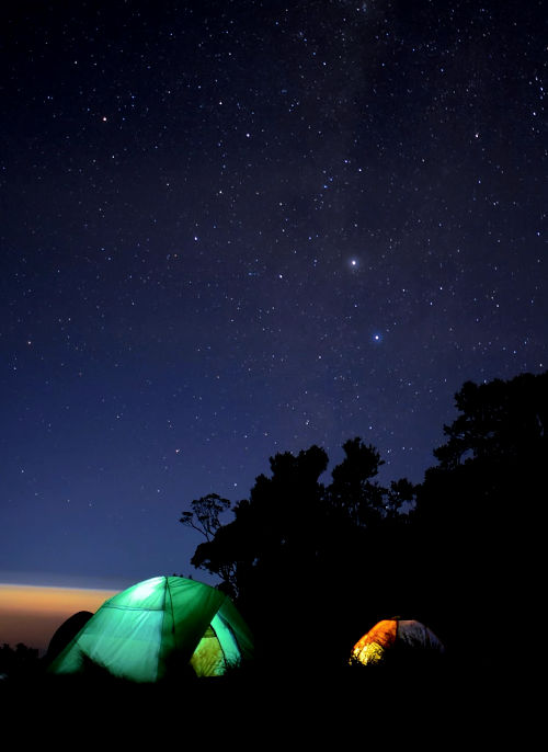 Illuminated green and orange tent under a starry sky.