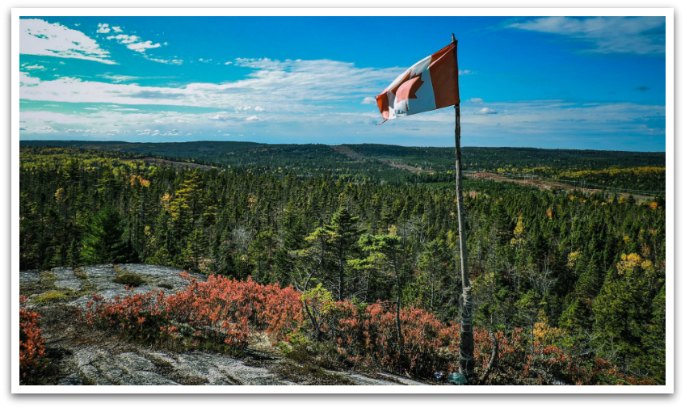 Canadian flag flying from a rock point with views of forests below.
