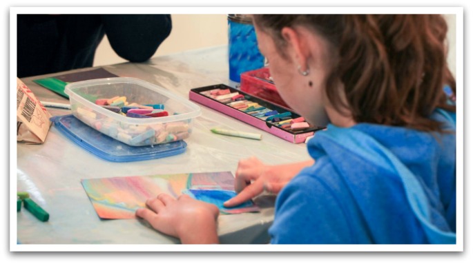 Girl drawing with chalk smudging her drawing.