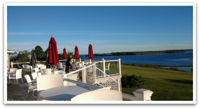 Chester Golf Clubhouse Restaurant's patio with red umbrellas over white tables and chairs facing blue waters on a sunny day.