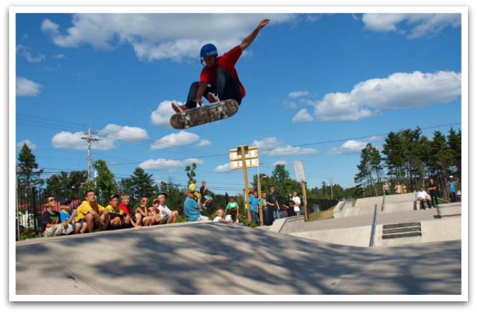 man mid air on a skateboard at the Chester skate park while a group of kids watch
