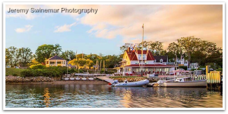 View from ocean of Chester Yacht Club at golden hour showing bandstand to the left and the white red roofed yacht club with trees in the background.