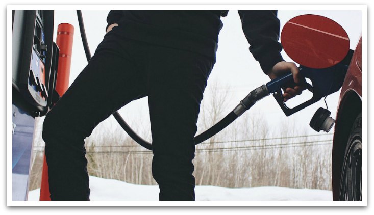 Person wearing black sweatpants with one hand in their pocket the other pumping gas into their vehicle.