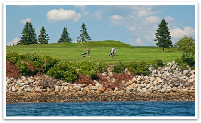 Four people carrying golf clubs on golf green by the ocean, photo taken from ocean.