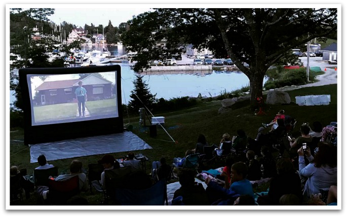 People sitting on picnic blankets watching Neapolian Dynamite  facing a wharf with many boats.