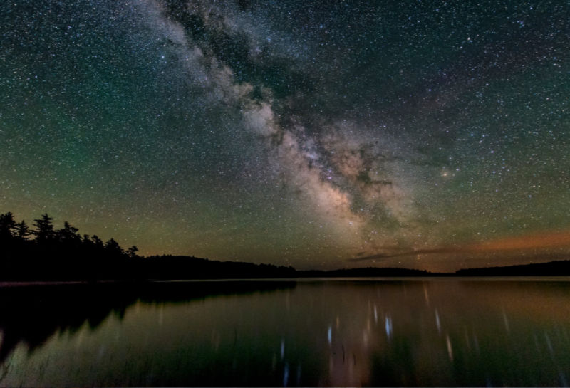 Lake surrounded by trees reflecting the milky way sky