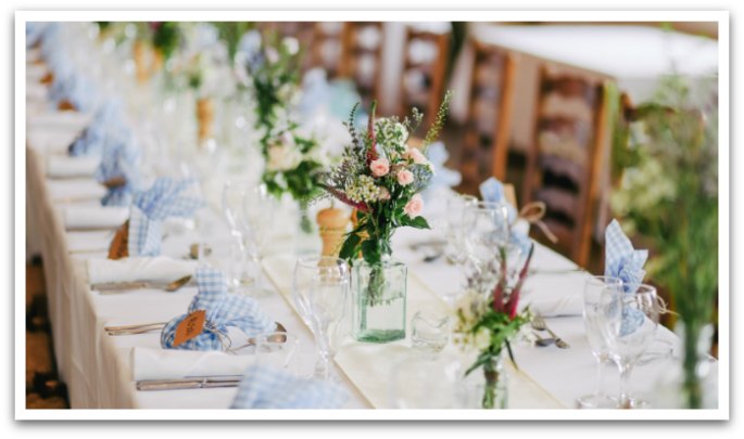 Long rectangular table with a white table cloth and bouquets as centre pieces.