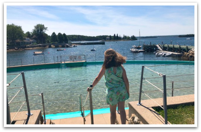 lady going in to the lido pool with harbour in the background