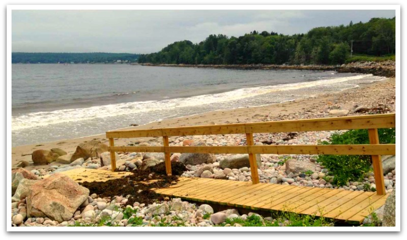 Small sand and rock beach leading onto sheltered ocean. Wooden ramp leading to it.