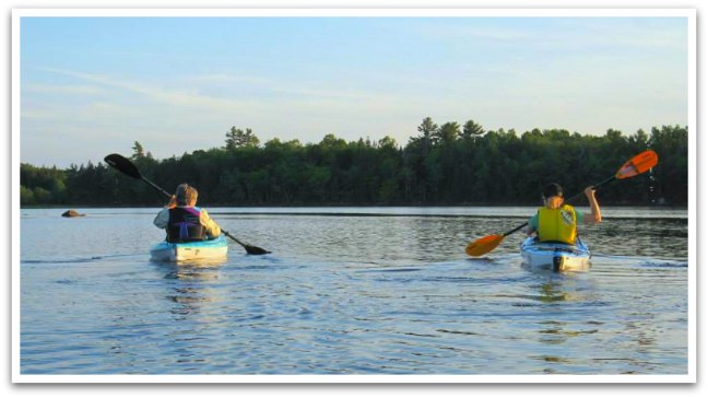 Two people paddling in kayaks on a lake.