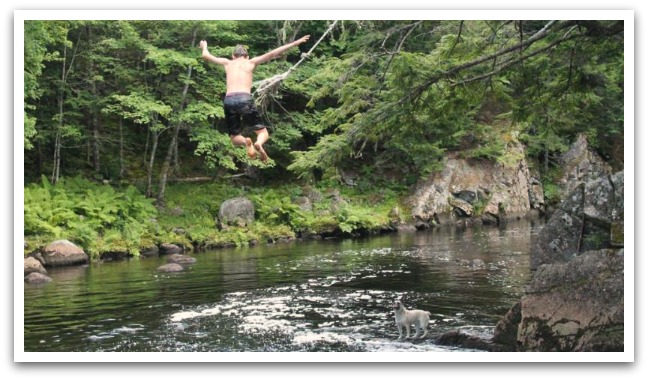 Boy jumping into a river surrounded by rocks and trees.
