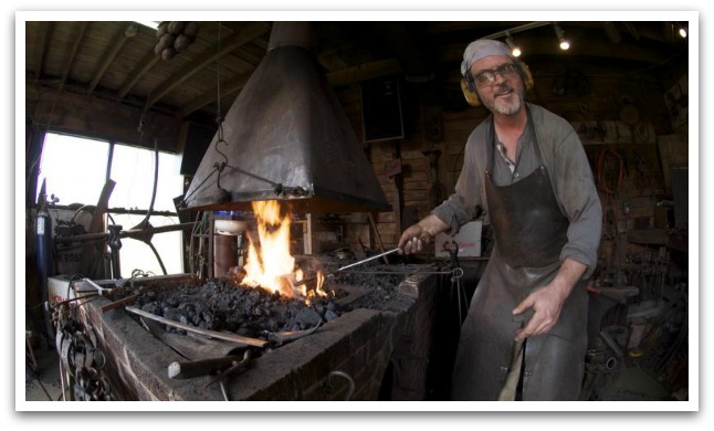 Man blacksmithing next to an open fire.