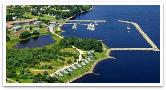 Bird's eye view of the Oak Island Resort showing hotel building, a wharf, tennis courts, the ocean, a lake, and greenery.
