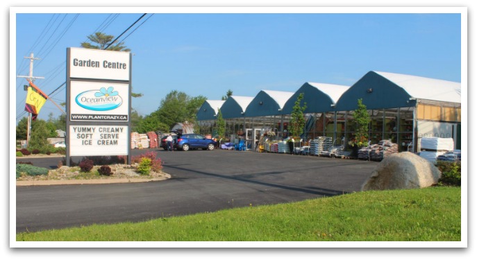 Exterior of Oceanview: a building with a wall of windows facing its car park with trees and bags of soil by the wall. Sign by the road exit reads "Garden centre. Oceanview".