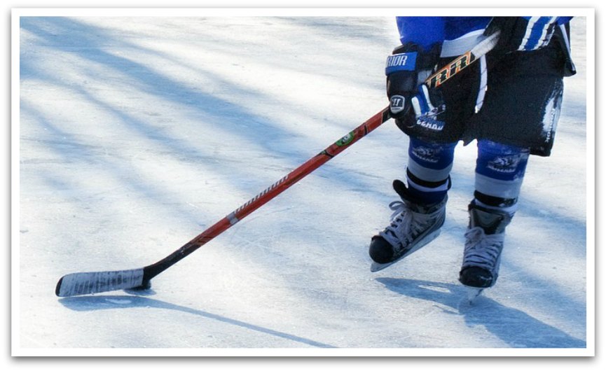 Waist down of hockey player wearing blue holding a hockey stick skating on ice.
