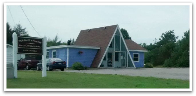 Peasant's Pantry exterior. Building is triangular and blue. A sign is in front reading "Peasant's Pantry. Specialty meats and deli. eat in / take out ".