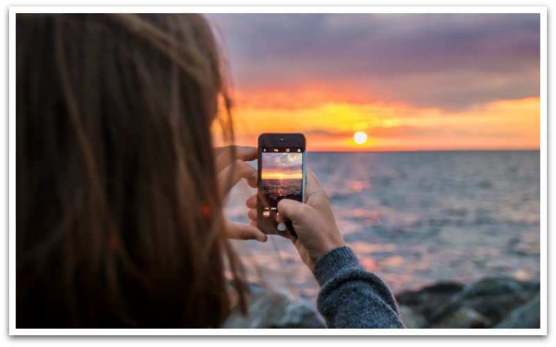 person taking a photo of the sunset on their phone