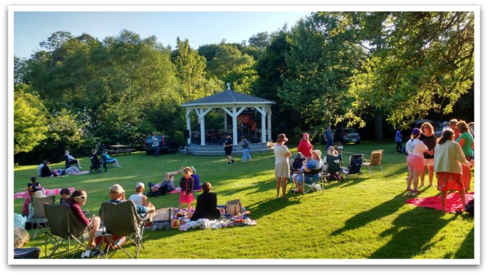 A bunch of families sitting on lawn chairs and picnic blankets around a gazebo in Lordly Park.