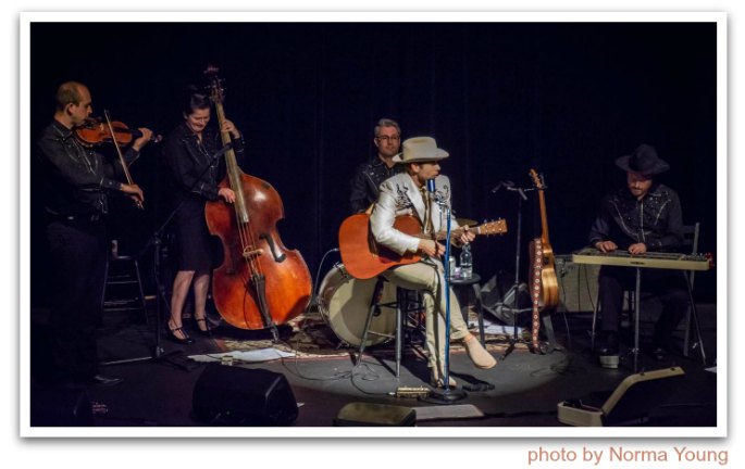 Group wearing Latin American suits playing string instruments on a stage.