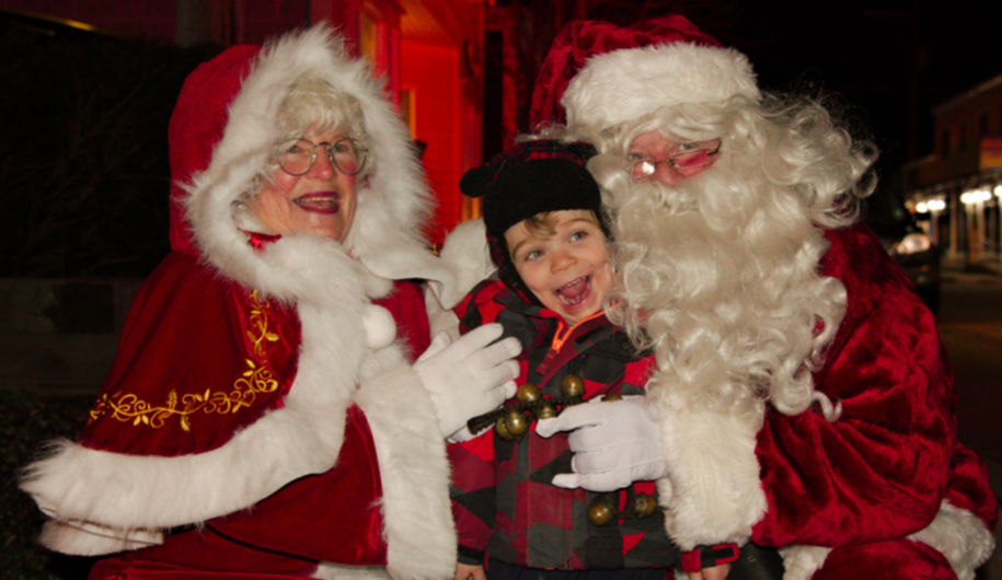 Photo of a child sitting on Santa's lap with Mrs Claus next to them