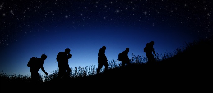 Silhouettes of people walking up a grassy hill at night under stars. 