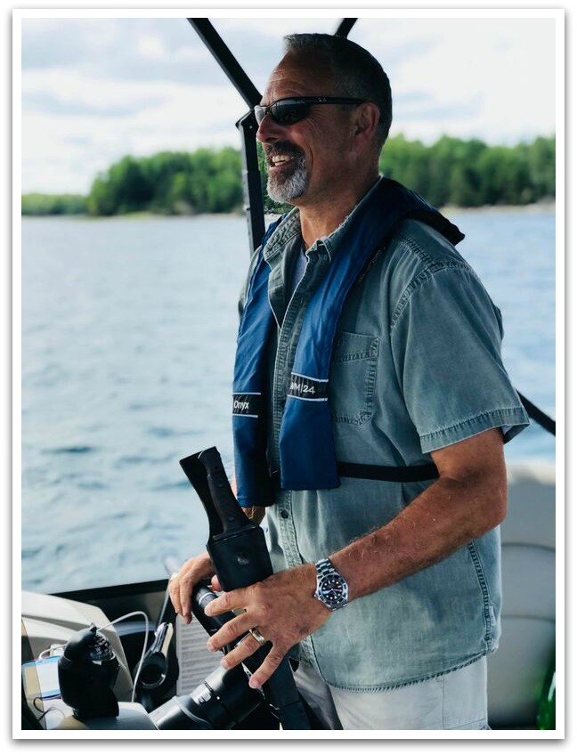Man smiling wearing a blue life vest and sun glasses steering the boat.
