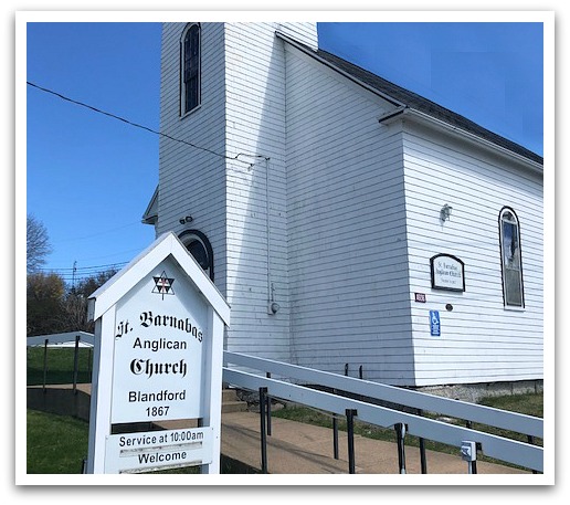 White church with ramp and sign outside reading "St. Barnabas Anglican Church. Blandofrd 1867, Service at 10:00 am. Welcome."