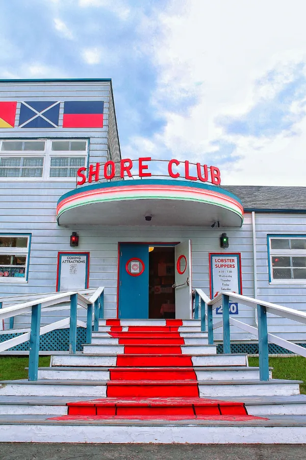 Photo of the entrance to the Shore Club, white stairs with railings on either side up to an open door with the Shore Club sign above.